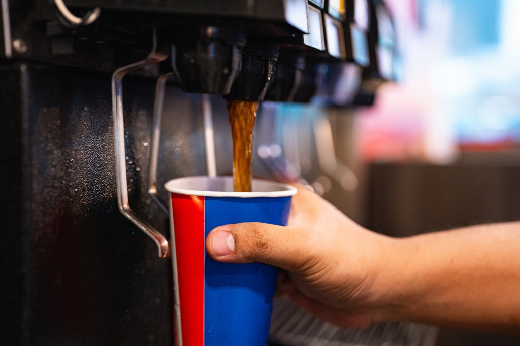 Person füllt einen Becher mit Cola auf.