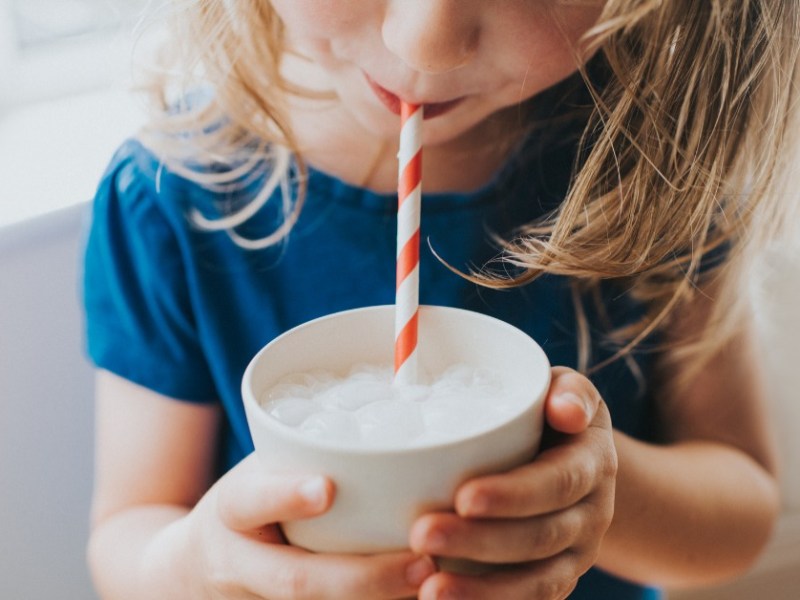 ein kleines Mädchen trinkt ein Getränk durch einen Papierstrohhalm