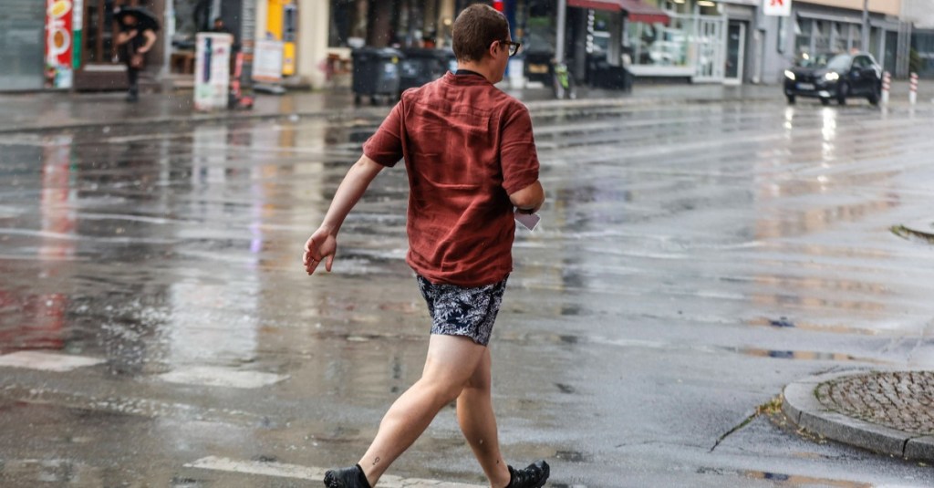 junger Mann rennt im Regen über die Straße