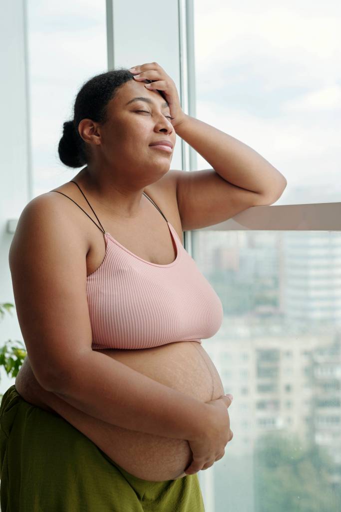 Schwangere Frau hält sich den Kopf und den Bauch