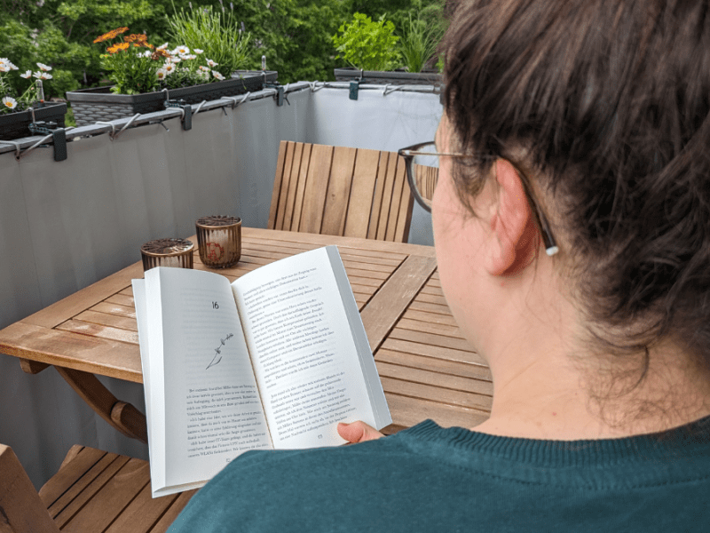Eine Frau liest ein Buch auf einem Balkon.