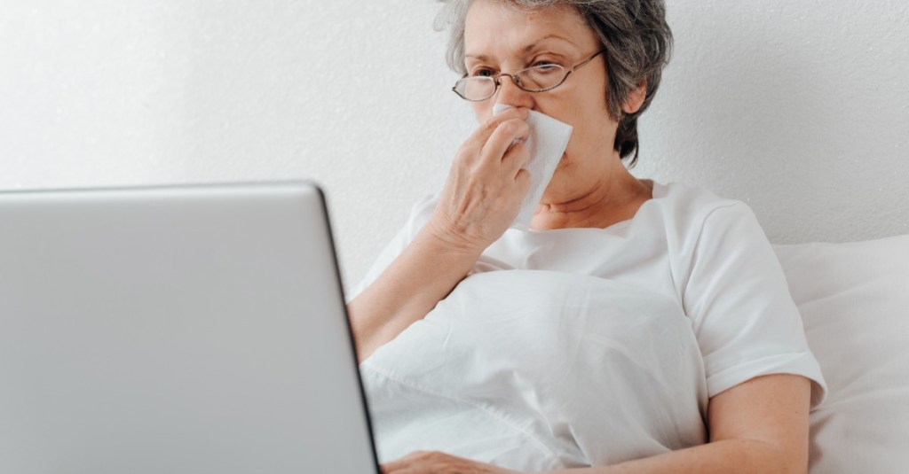 Frau liegt krank im Bett und schaut auf einen Laptop