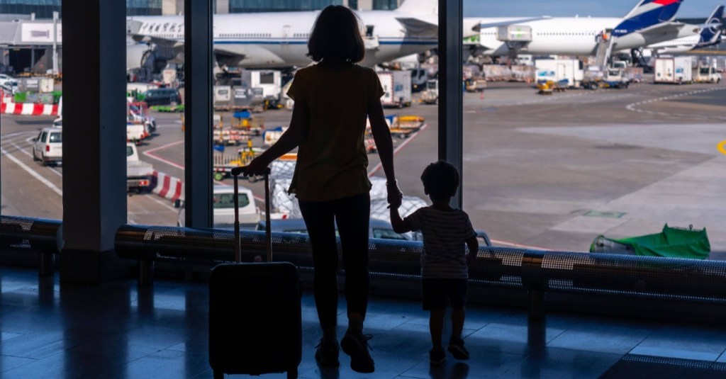 Mutter steht mit Kind an einem Terminal und betrachtet ein Flugzeug