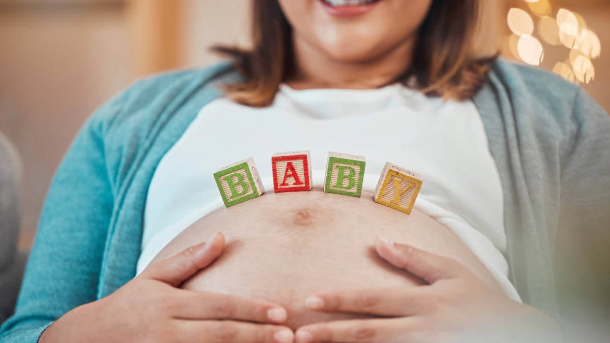 Schwangere Frau hält ihre Hände am Bauch, auf diesem stehen Würfel mit dem Wort Baby.
