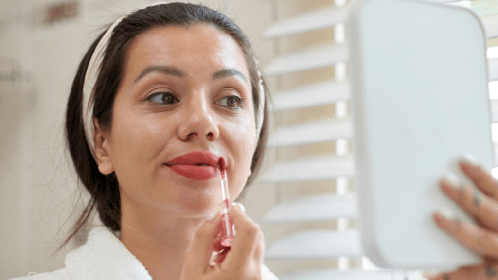 Eine Frau trägt flüssigen Lippenstift mithilfe eines Handspiegels auf.