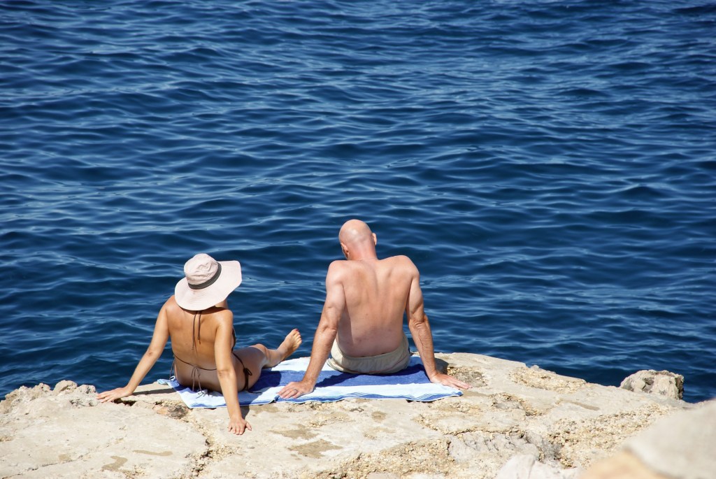 Frau mit Sonnenhut und Mann mit Glatze nehmen ein Sonnenbad.