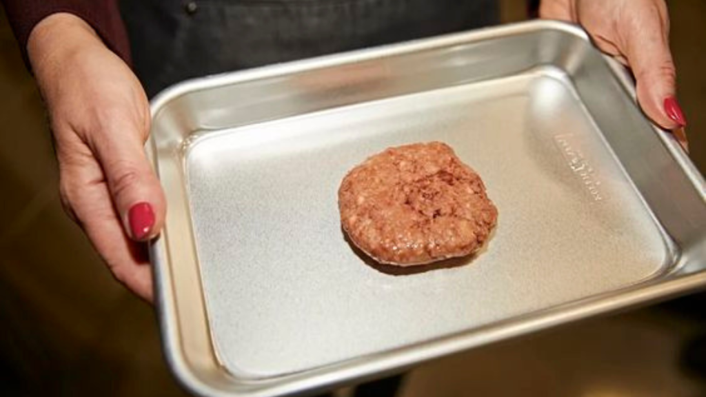 Eine Person hält ein silbernes Tablett in der Hand, auf dem ein Fleisch-Patty liegt.