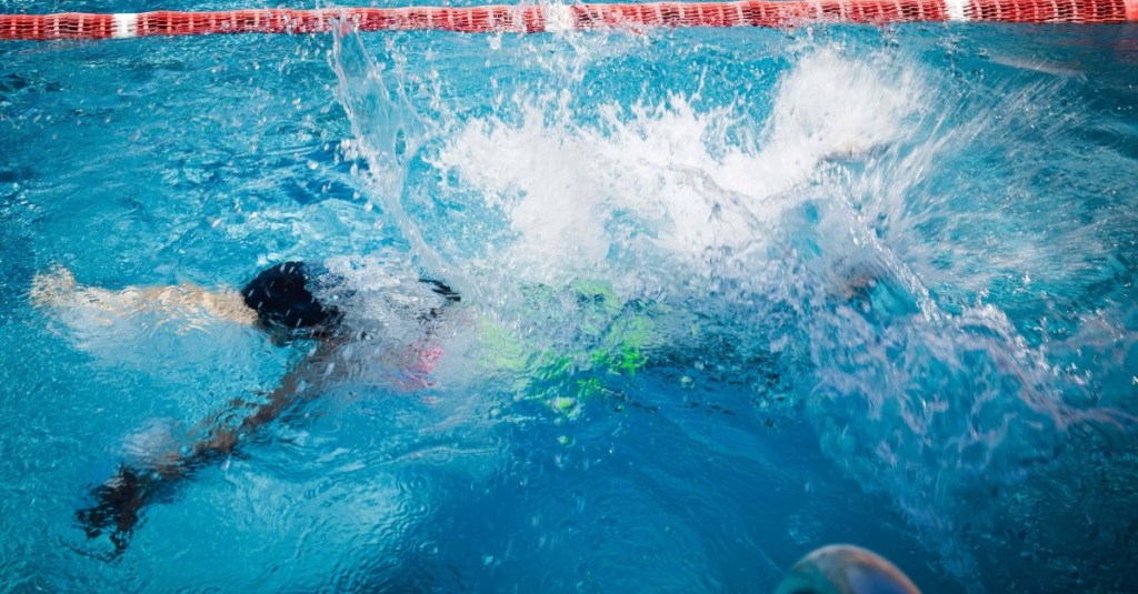 Kind mit neonfarbenen Badesachen schwimmt unter Wasser