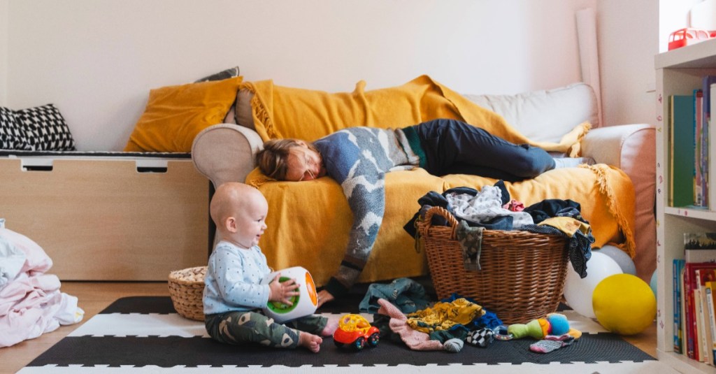 Kleines Kind spielt im Kinderzimmer, während die müde Mama auf dem Sofa schläft.