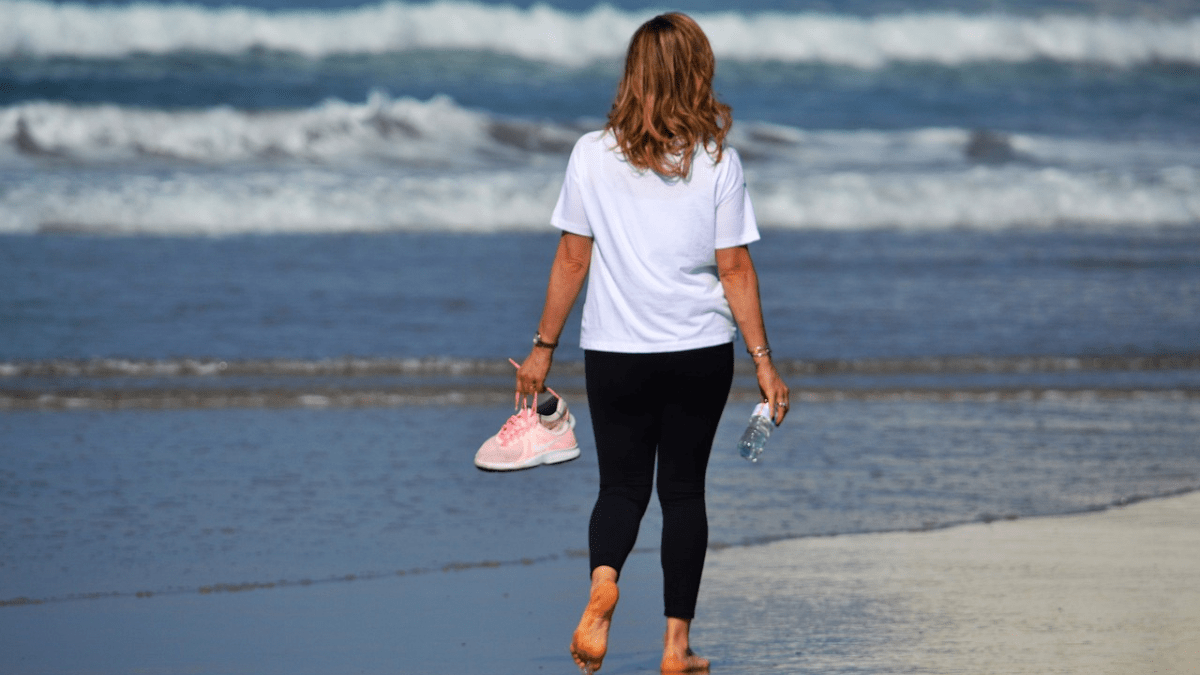 Eine Frau steht mit dem RÃ¼cken zur Kamera am Strand und blickt auf das Wasser.