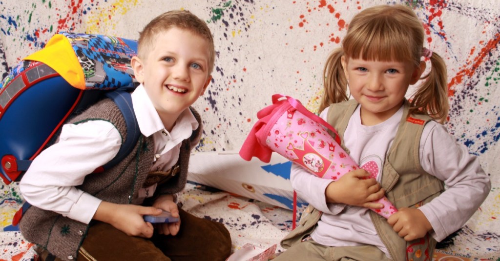 ein Junge mit Schulranzen und ein kleines Mädchen mit einer Zuckertüte sitzen auf dem Boden