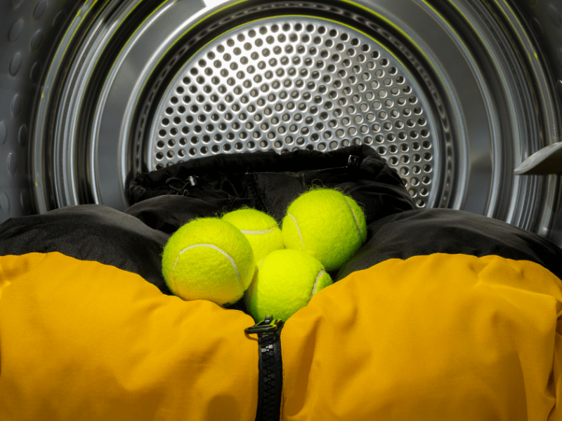 Tennisbälle liegen in einer Waschmaschine auf einer Daunenjacke.