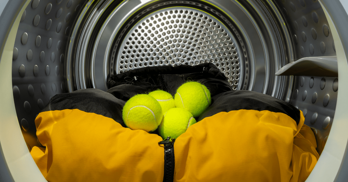 Tennisbälle liegen in einer Waschmaschine auf einer Daunenjacke.