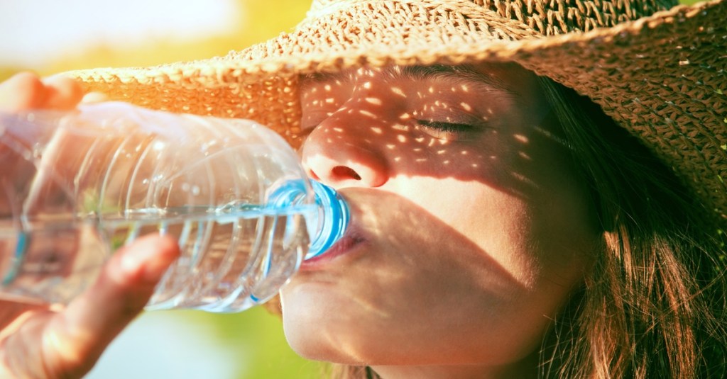 Frau mit Sonnenhut trinkt Wasser.