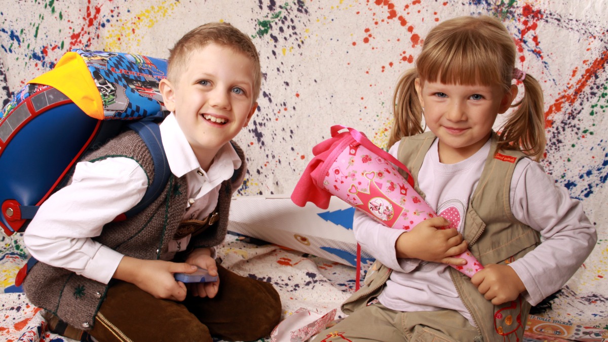 ein Junge mit Schulranzen und ein kleines Mädchen mit einer Zuckertüte sitzen auf dem Boden