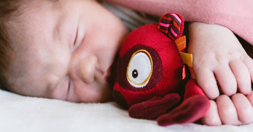 Ein Baby liegt mit einem Kuscheltier im Bett.