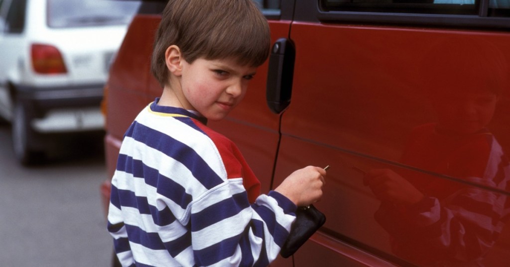 Kleiner Junge macht sich mit einem Schlüssel an einem Autolack zu schaffen