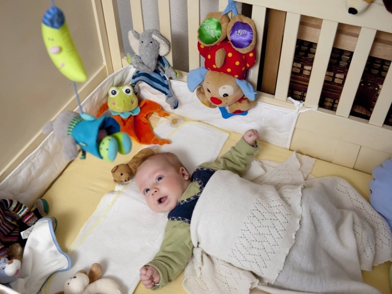 Baby liegt mit Spielzeug und Kuscheltieren in seinem Bett.