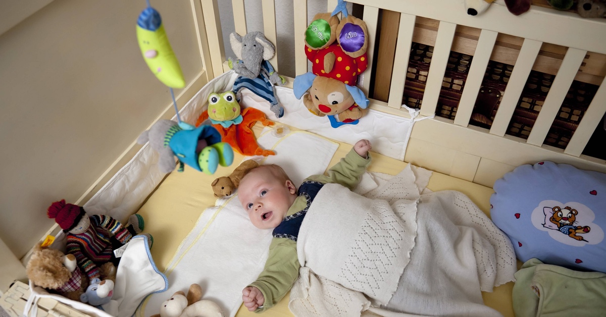 Baby liegt mit Spielzeug und Kuscheltieren in seinem Bett.