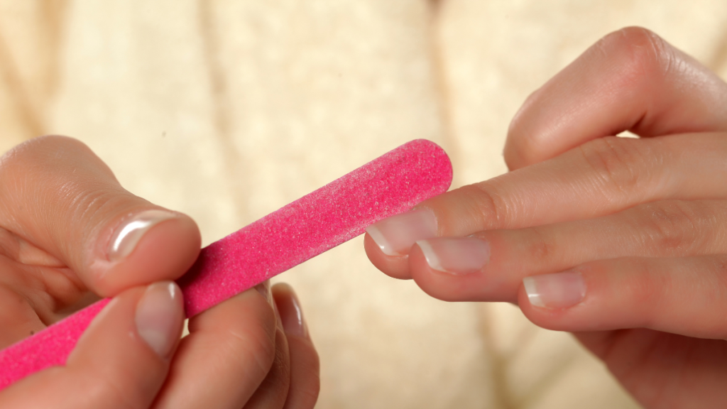 Eine Person feilt ihre Nägel mit einer pinken Nagelfeile.