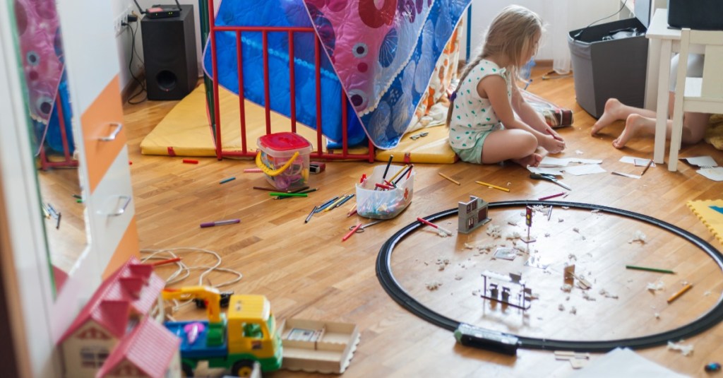 Ein Mädchen sitzt in ihrem Kinderzimmer, das unaufgeräumt ist.