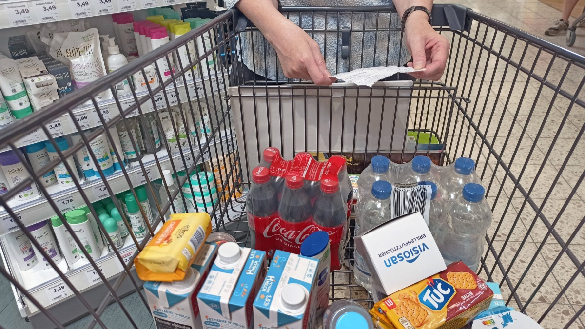 Frau mit Einkaufszettel stützt sich auf einen gut gefüllten Einkaufswagen.