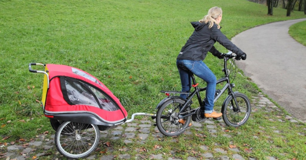 Eine Mutter fährt mit ihrem Fahrrad, an dem ein Fahrradanhänger mit einem Kind hängt.