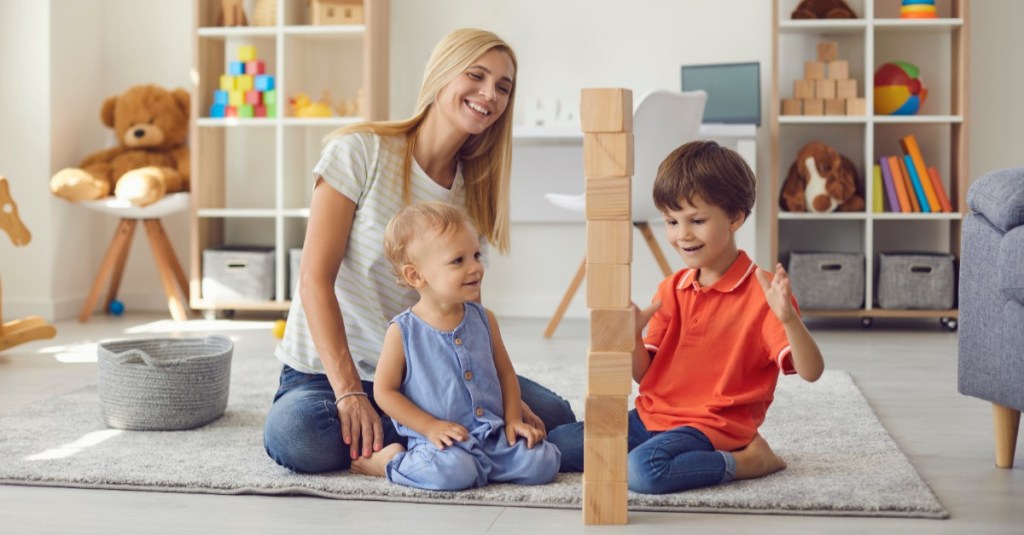 Mutter baut mit ihren zwei Kindern einen Turm aus Holzbausteinen