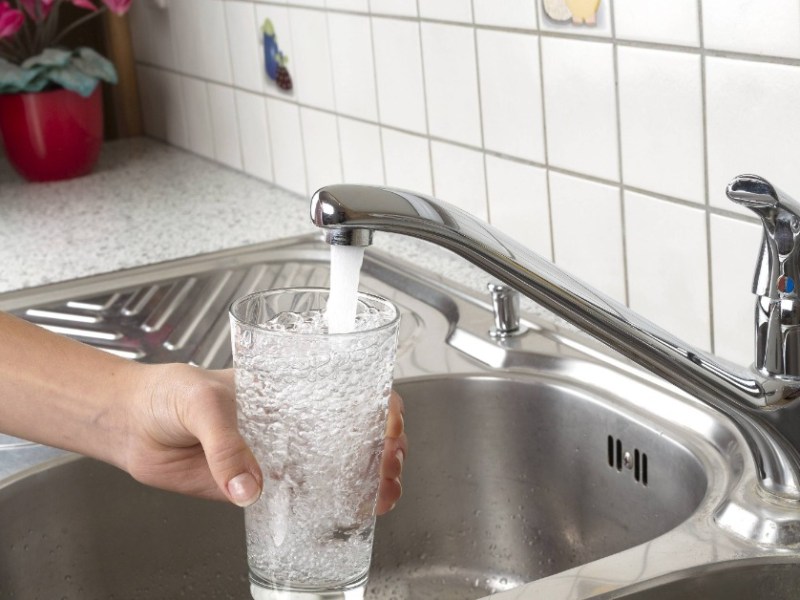 Jemand hält ein Glas unter einen Wasserhahn in der Küche und füllt es mit Wasser.