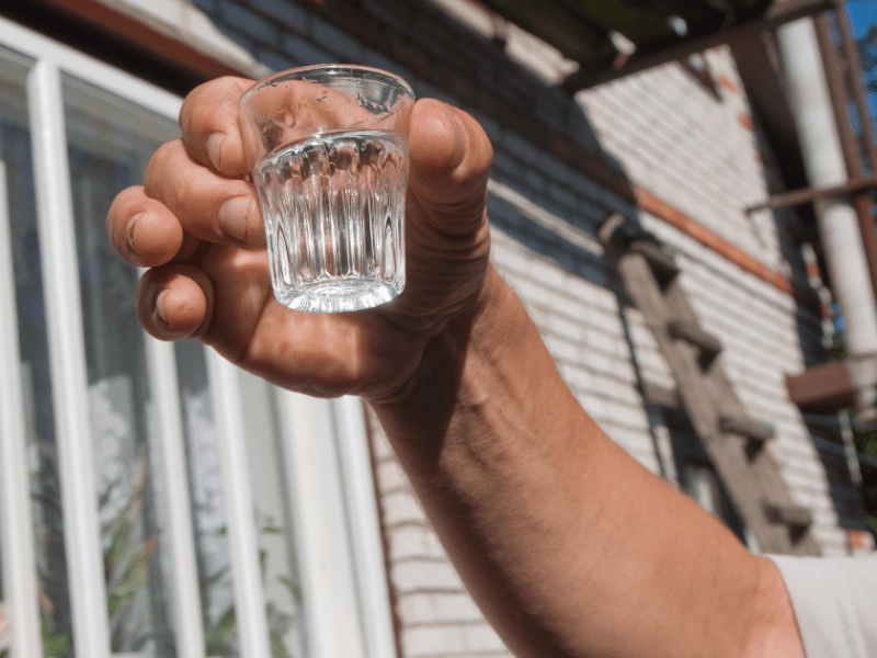 Eine Person hält ein Schnapsglas mit Wodka in die Luft.