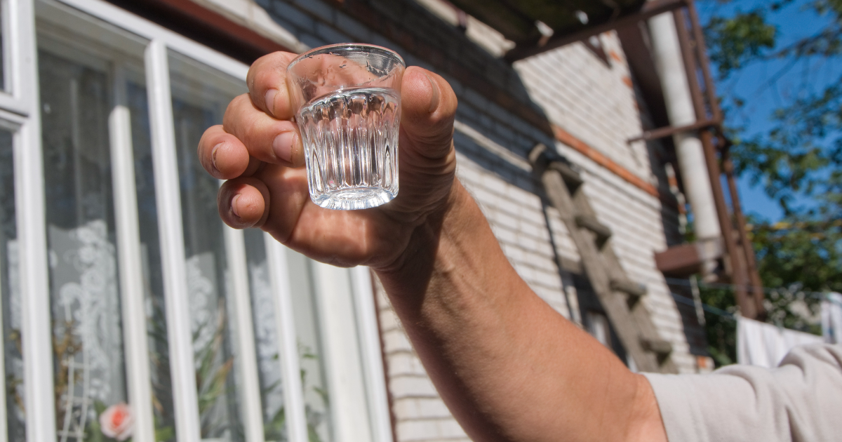 Eine Person hÃ¤lt ein Schnapsglas mit Wodka in die Luft.