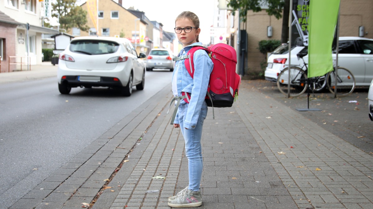 sicherer Schulweg: ein MÃ¤dchen mÃ¶chte eine viel befahrene StraÃŸe Ã¼berqueren