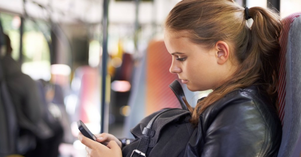 Jugendliche sitzt im Bus und schaut auf ihr Handy