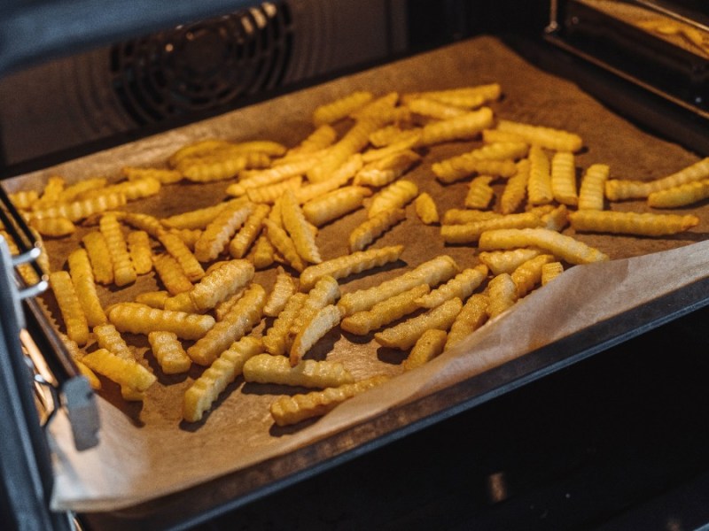 Pommes auf Backpapier auf einem Blackblech im Ofen