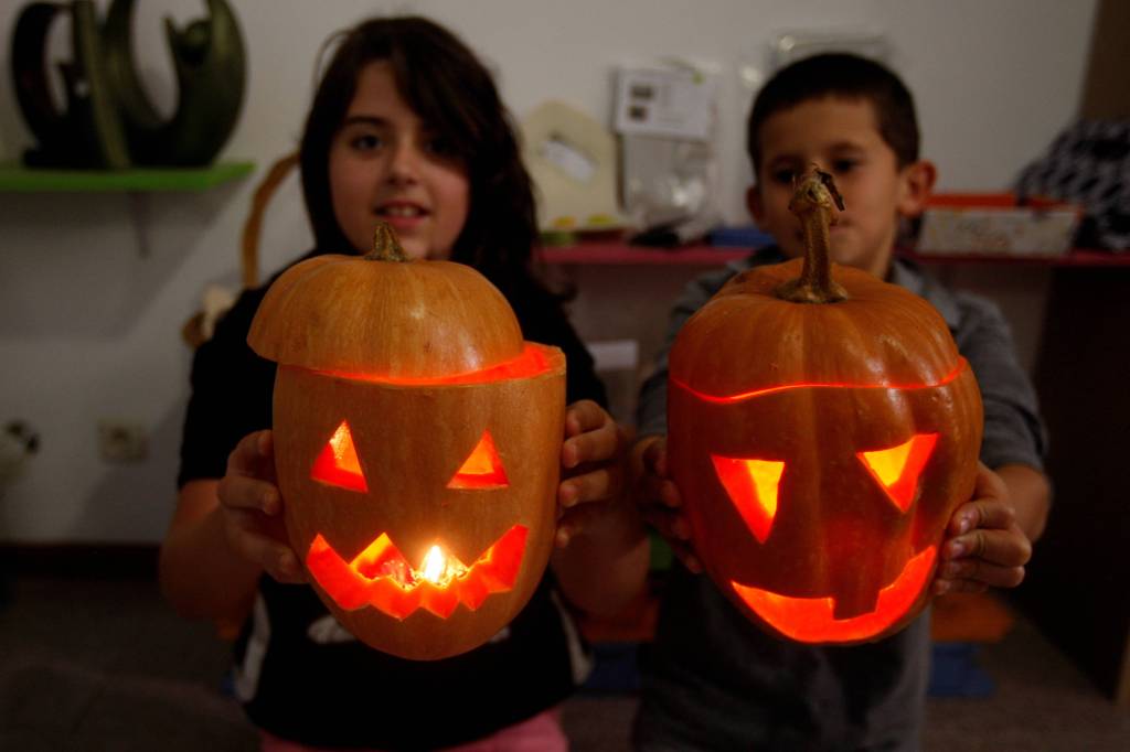 Zwei Kinder halten ihre geschnitzten, beleuchteten Halloweenkürbisse hoch.