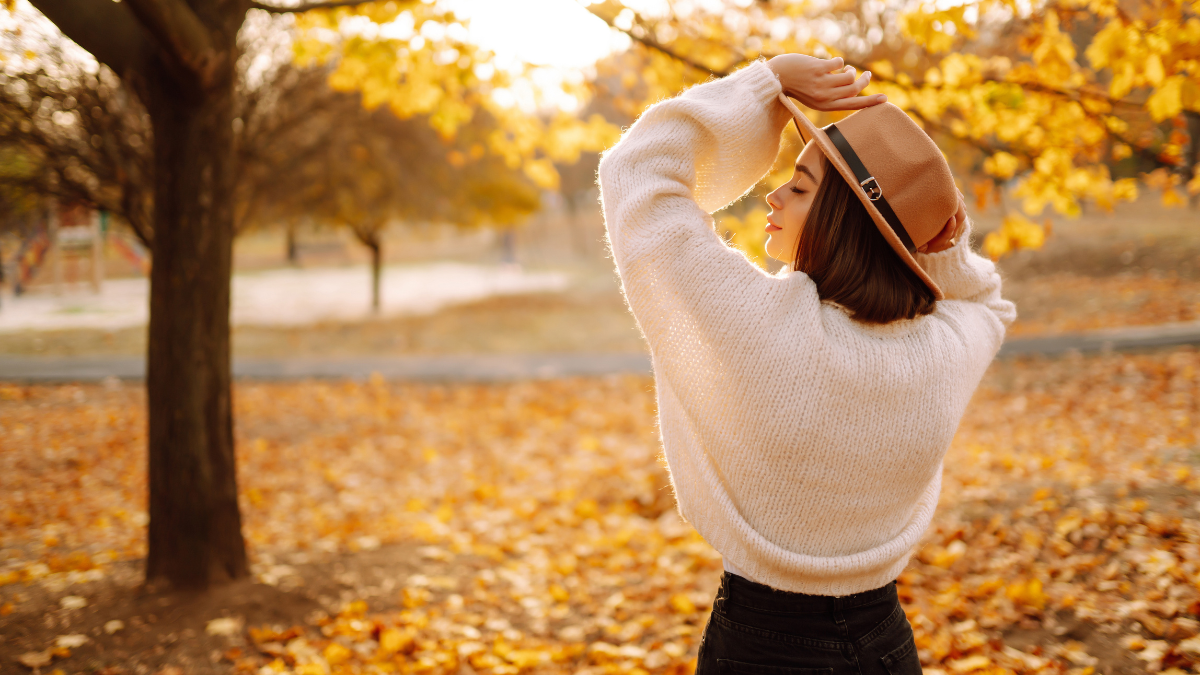 Eine Frau mit Hut in einer herbstlichen Landschaft.