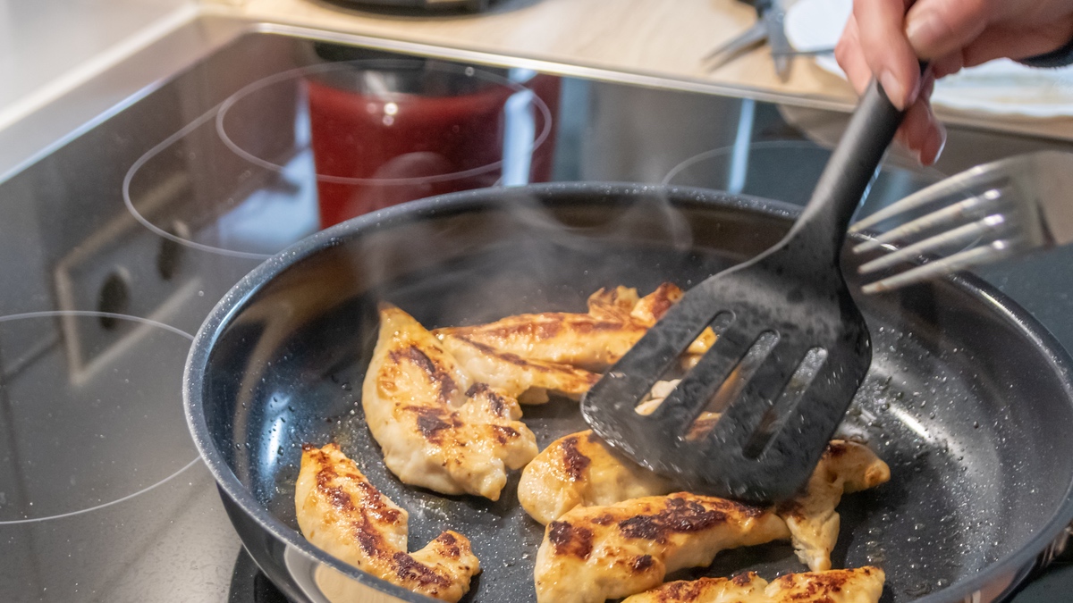 Hähnchen anbraten mit schwarzem Pfannenwender.