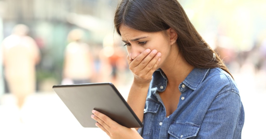 junge Frau blickt erschrocken auf ihr Tablet