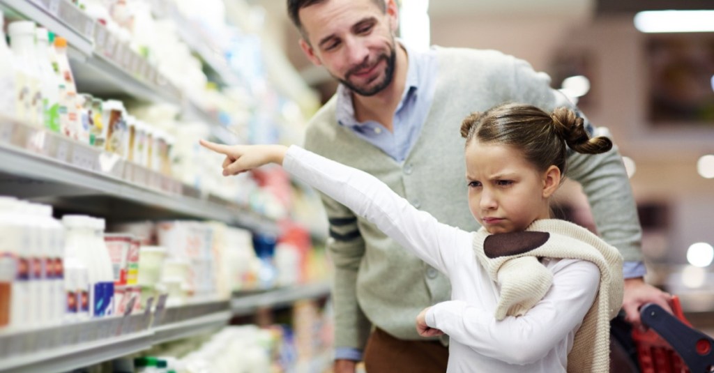 Mädchen zeigt bockig im Supermarkt auf ein bestimmtes Produkt