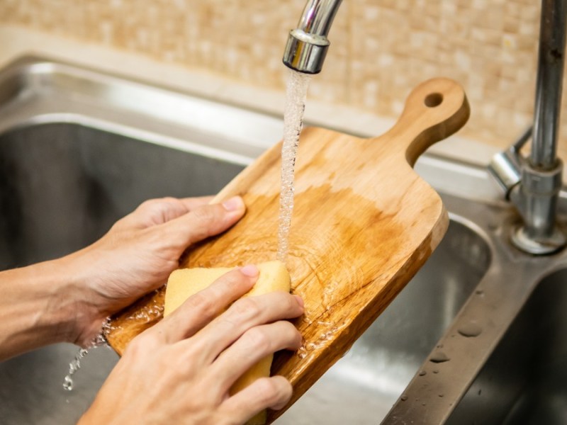 Holzbrett reinigen: eine Frau wäscht ein Holzbrett unter fließendem Wasser