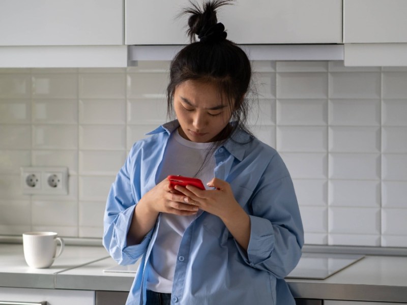 eine junge Frau steht in der Küche und tippt in ihr Telefon