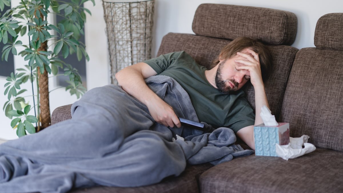 Ein Mann liegt auf dem Sofa und hÃ¤lt sich seinen schmerzenden Kopf.