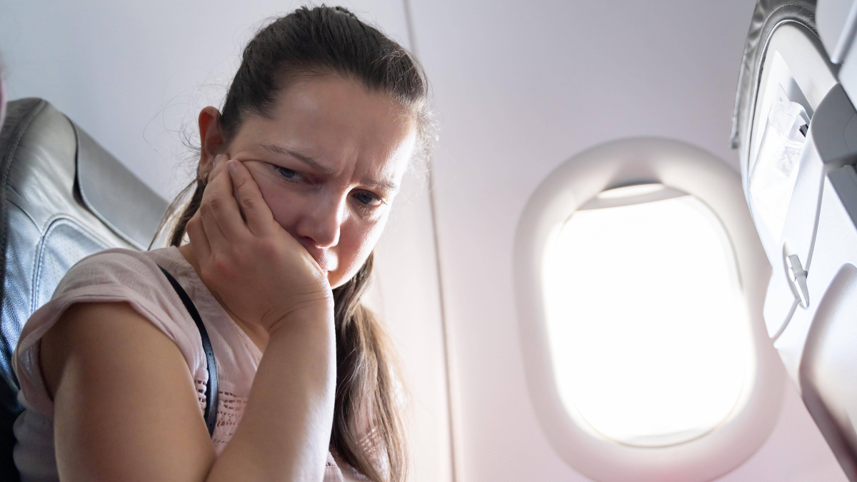 Frau mit Flugangst sitzt im Flugzeug und hat den Kopf auf die Hand gestÃ¼tzt.