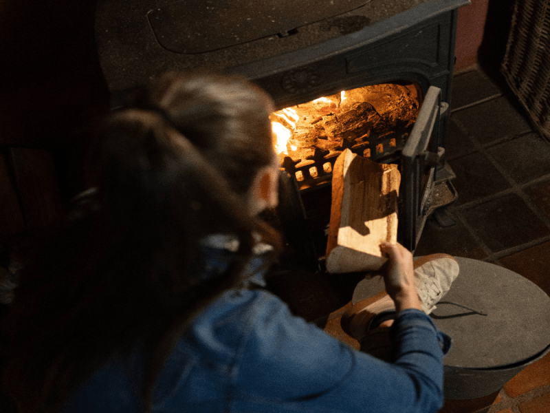 Eine Frau legt einen Holzscheit in einen Kamin.