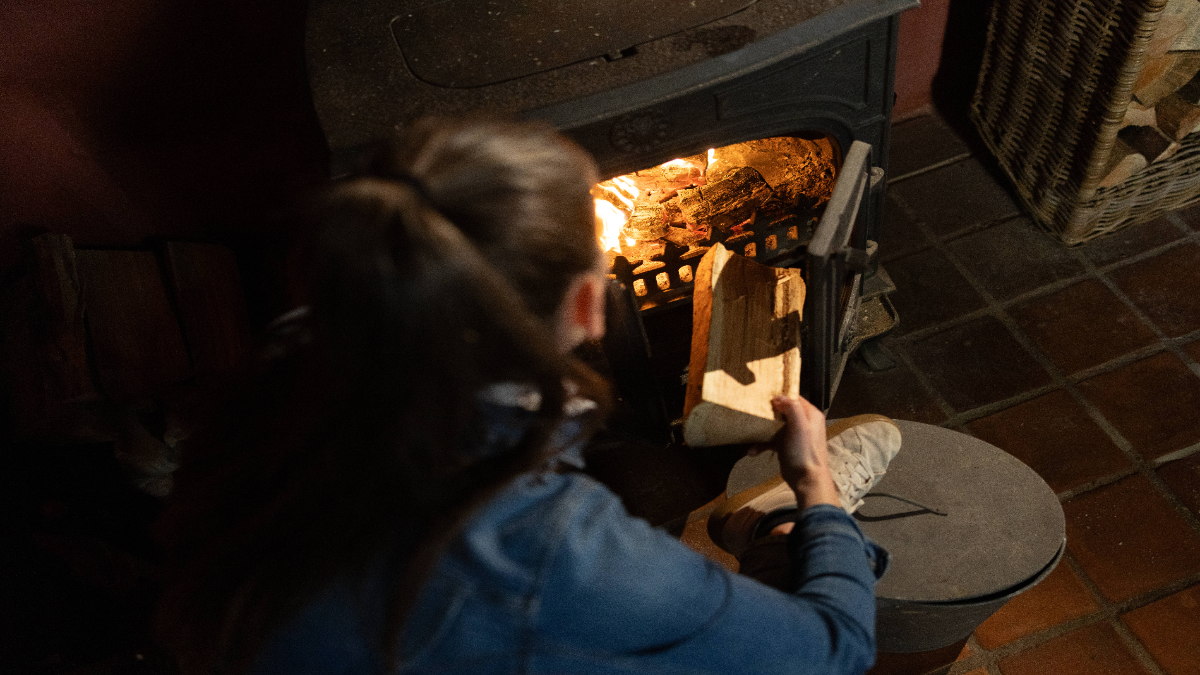 Eine Frau legt einen Holzscheit in einen Kamin.