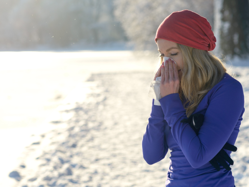 Eine Frau in Sportkleidung putzt sich im Freien die Nase.