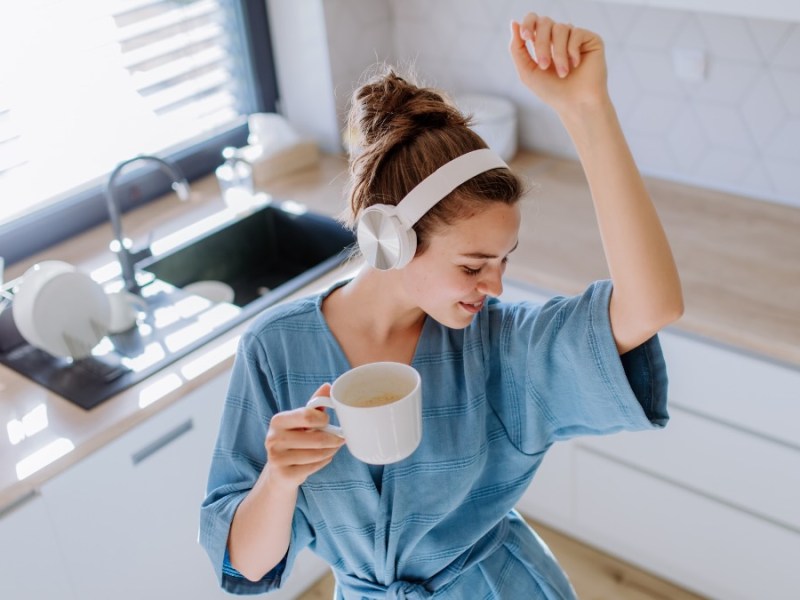 Eine Frau hat KopfhÃ¶rer auf und eine Tasse in der Hand und tanzt in ihrer KÃ¼che.