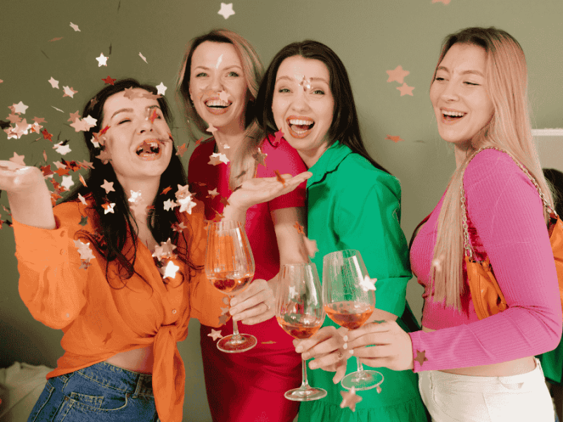 Galentine's Day, bunt gekleidete Frauen stoßen an und werfen Konfetti