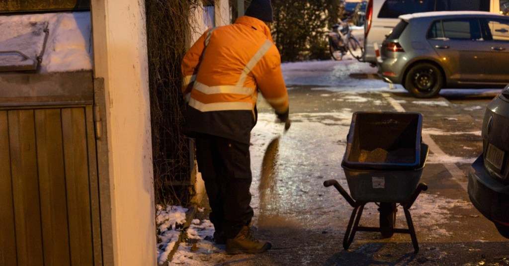 Schnee räumen: ein Mann wirft Streugut auf einen glatten Gehweg