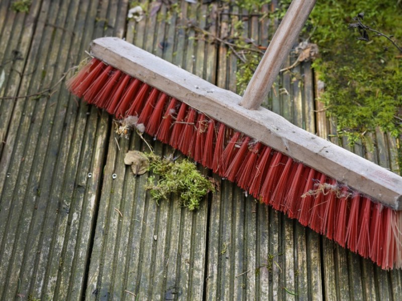 mit einem roten Besen wird eine Holzterrasse gereinigt